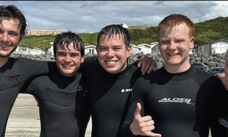 Five Rider students pose for a photo in their wet suits after surfing.