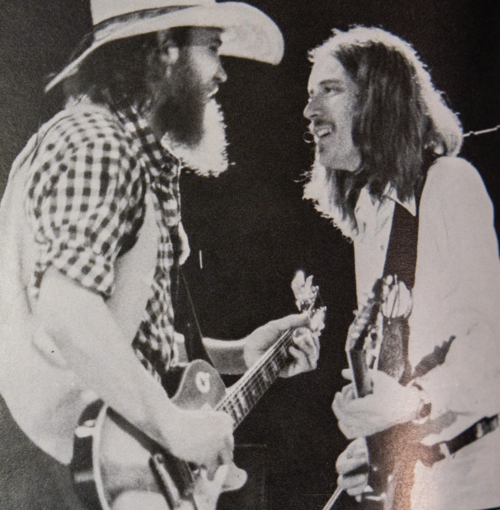 Two members of the Charlie Daniels Band chuckle while playing guitar.