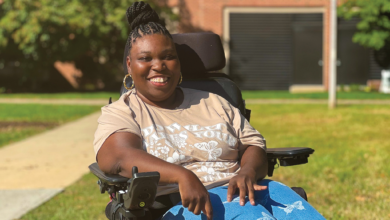Marlene sits in an electric wheelchair in front of an academic building