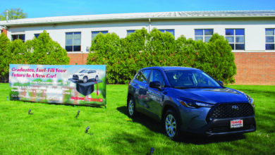 A gray-blue Toyota Corolla Cross L. sits on display on a lawn in front of a building.
