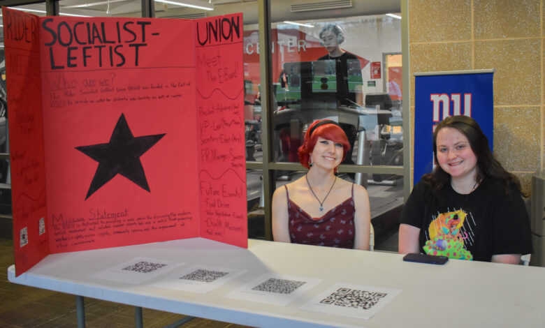 Spencer Nelson and Lex Wright sit at a table with QR codes and a poster with information on RSLU.
