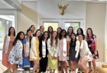 A group of women in the Gail Bierenbaum Leadership Council stand together for a picture in front of a window.